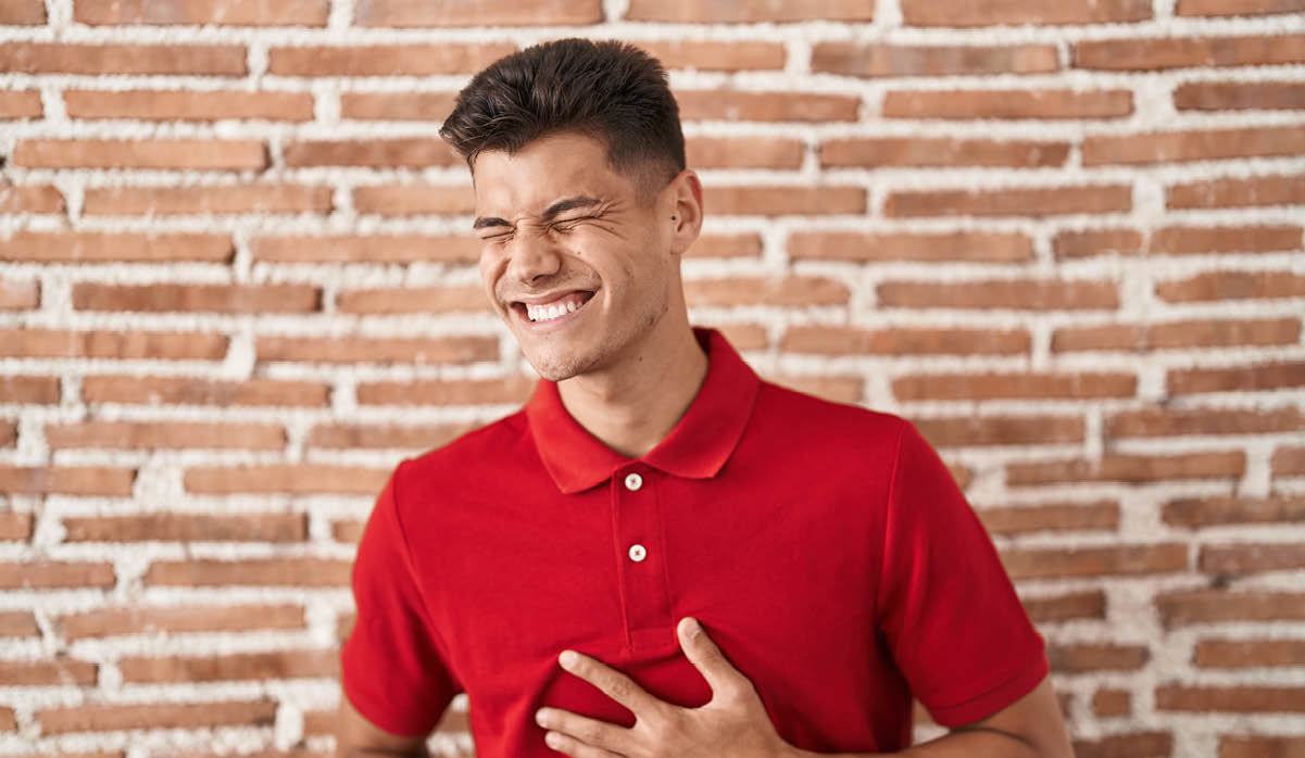 Young hispanic man standing over bricks wall with hand on stomach because indigestion, painful illness feeling unwell. ache concept. 