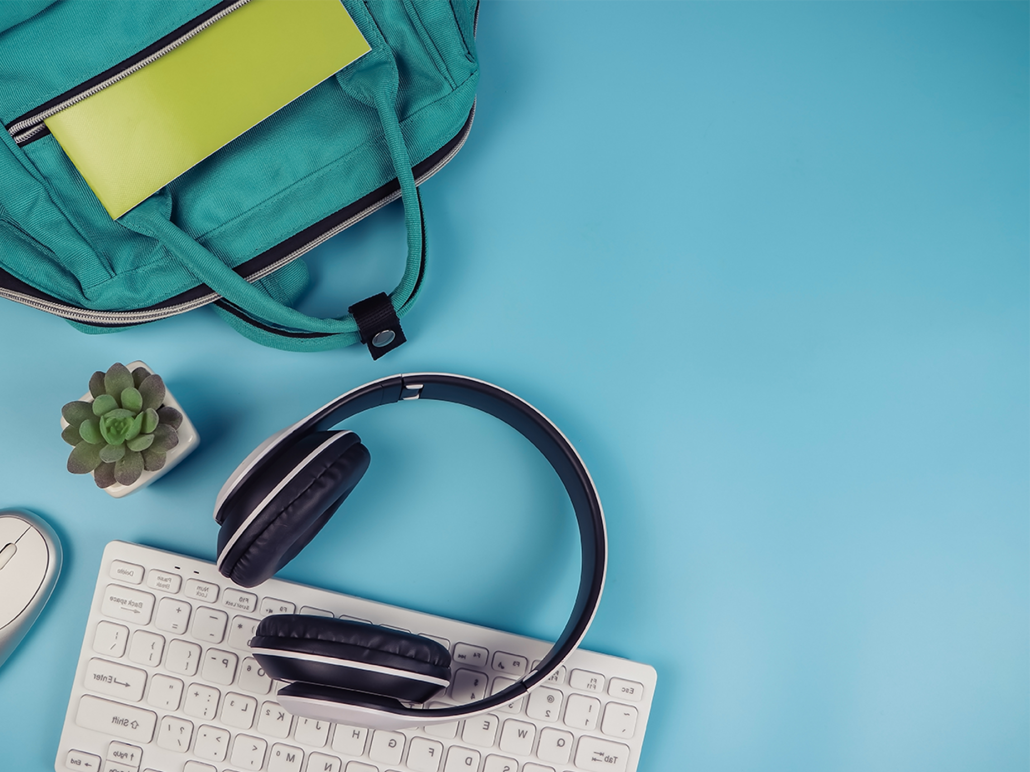 Top view or flat lay of headphones, computer keyboard, mouse, school backpack and cactus on blue background with copy space. Online learning concept.