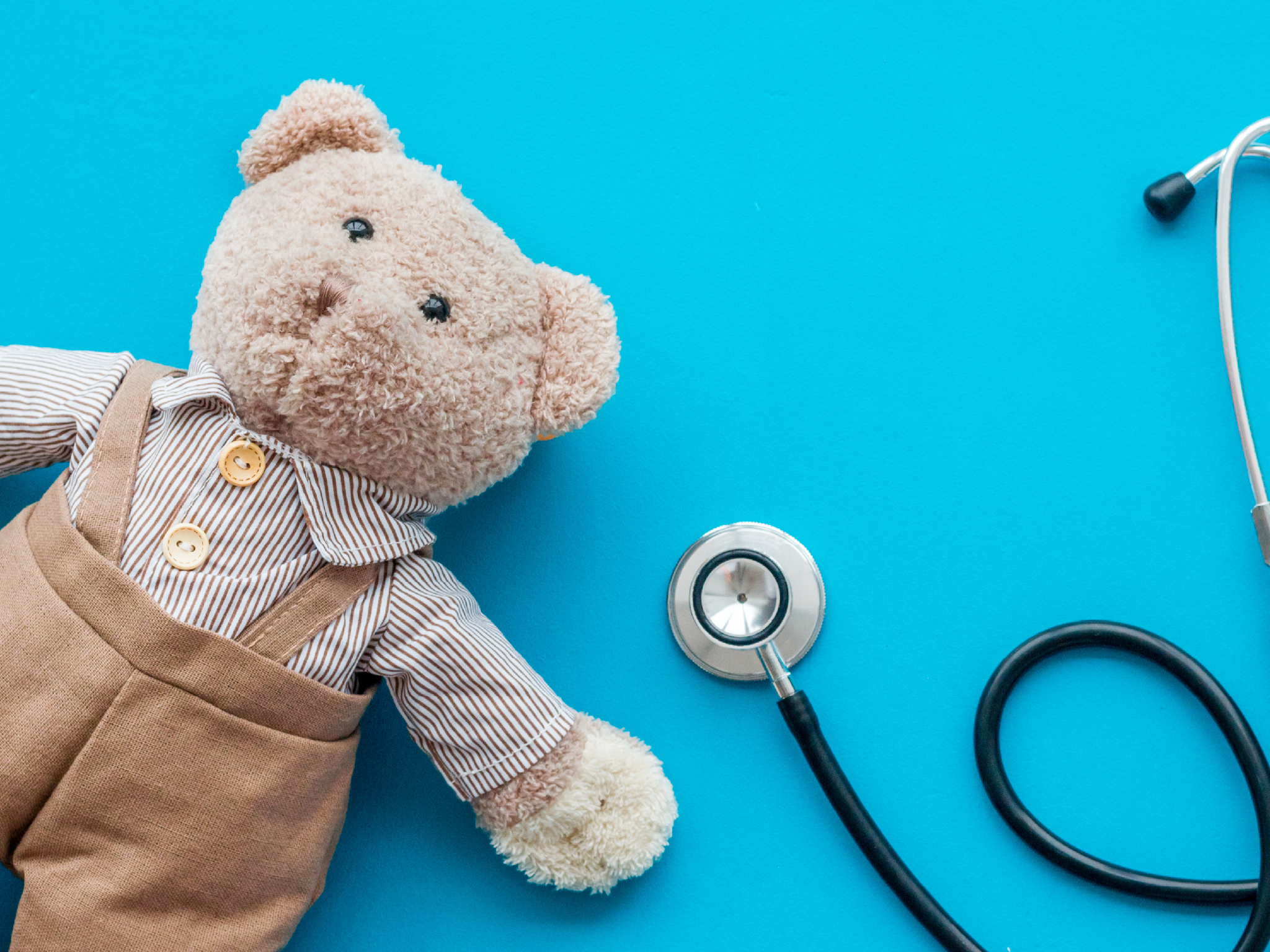 Children's doctor concept. Teddy bear toy and stethoscope on blue background top view.