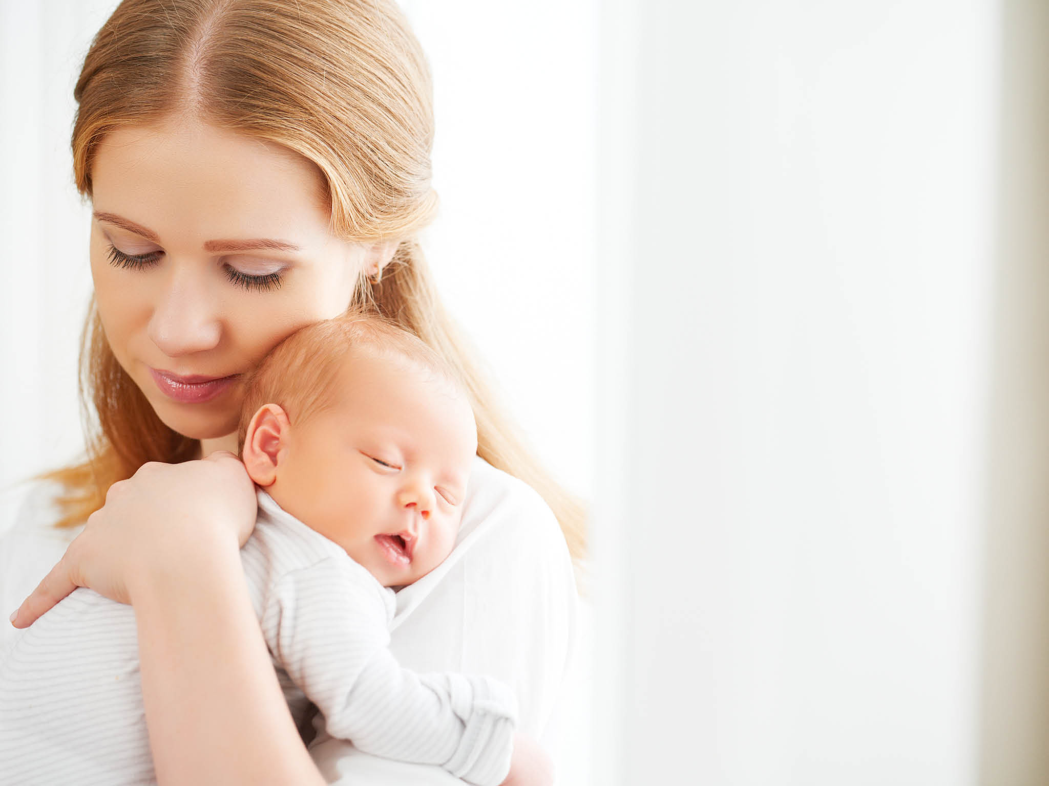 newborn baby in a tender embrace of mother at the window