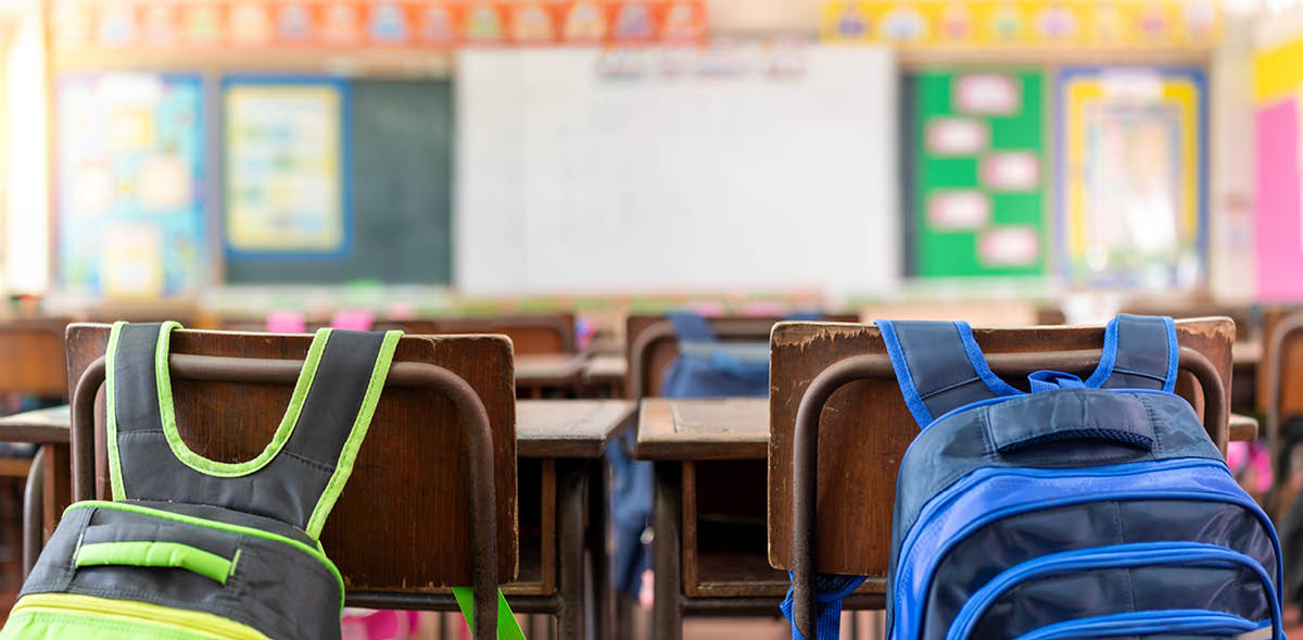 Empty classroom in elementary school with whiteboard and teacher's desk, school bag hanging on a chair.