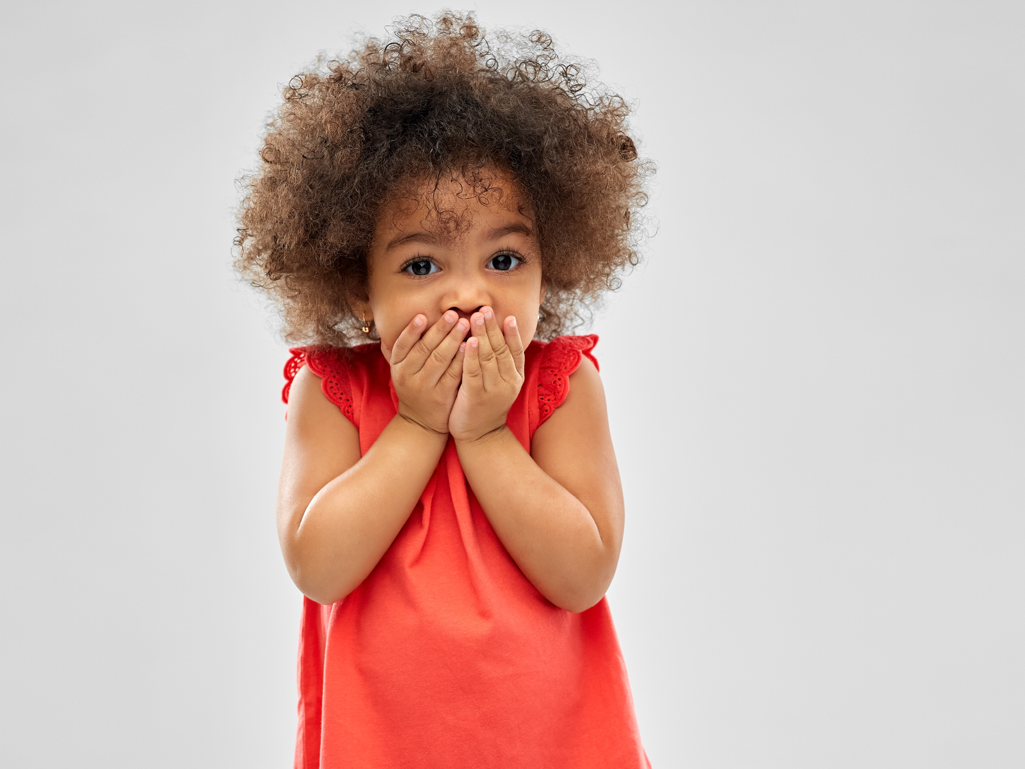 childhood, expression and emotion concept - confused little african american girl covering mouth by hands over grey background