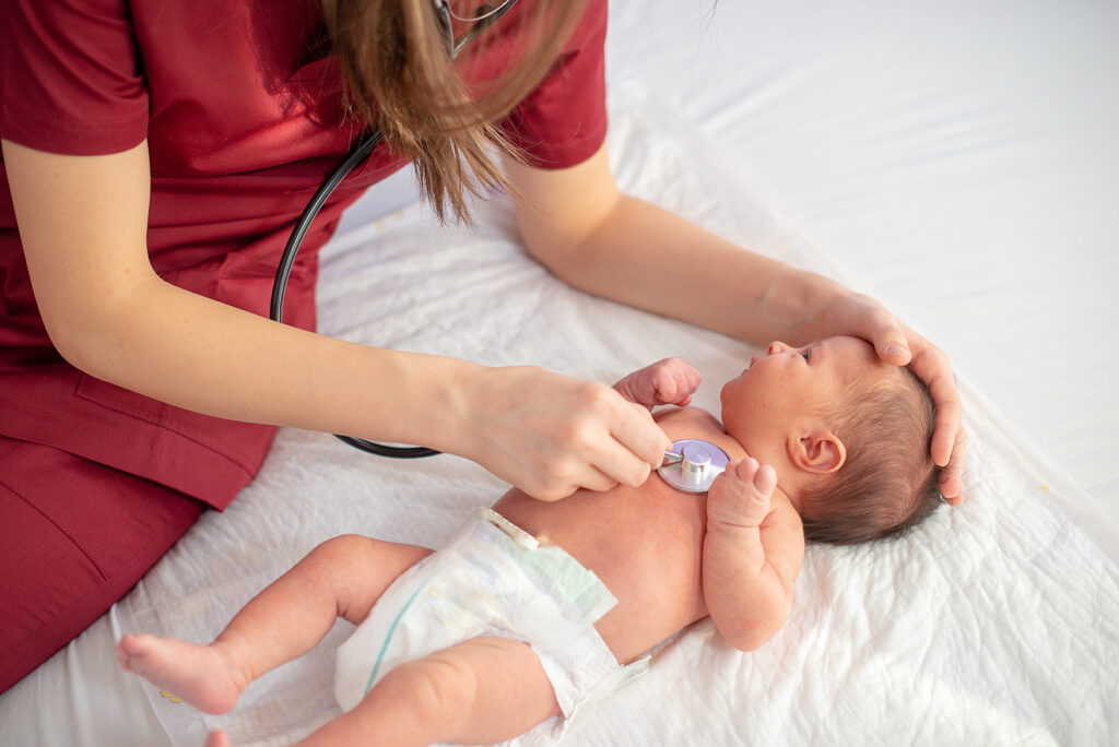 Pediatric doctor exams newborn baby girl with stethoscope in hospital.