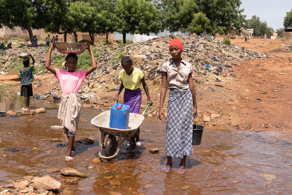 Group of African children transporting water from the public well with possible health impacts.